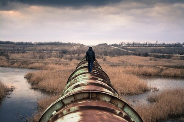 Energy photo of man in coat walking on pipeline across a field.