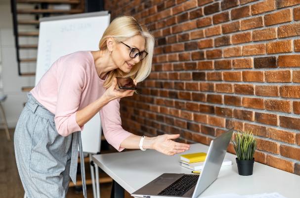 Death of a Spouse depicts attractive older woman speaking into mobile phone while looking at laptop.