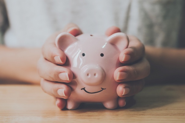 Investment Holdings shows women's hands holding piggy bank on wood table.