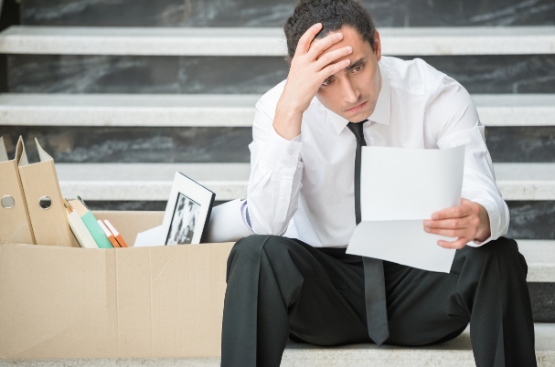 What to do after being laid off is depicted by a fired frustrated man in suit sitting at stairs in office.