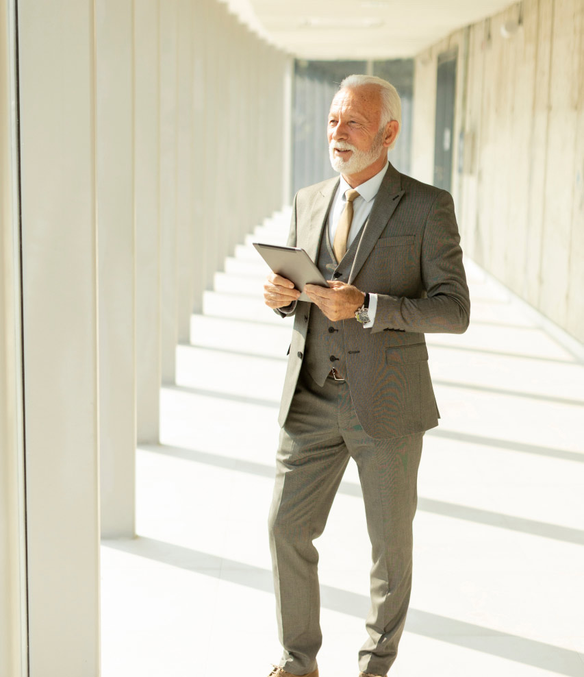 Wealth management and financial planning for high-net-worth individuals portrait concept of mature businessman standing in office hallway with digital tablet.