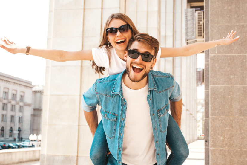 Next generation financial planning portrait with girlfriend playfully extending arms out while sitting on back of boyfriend.