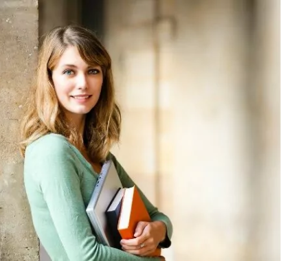 Guide to paying for college concept photo of a college-aged woman holding books while leaning against a cement pillar.