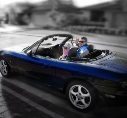 Preparing For retirement concept with middle-aged woman and man driving down the street in a shiny blue convertible car.