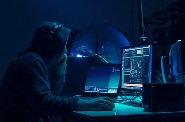 What you need to know about cybersecurity concept of a young hacker in a dark room reading a computer screen.