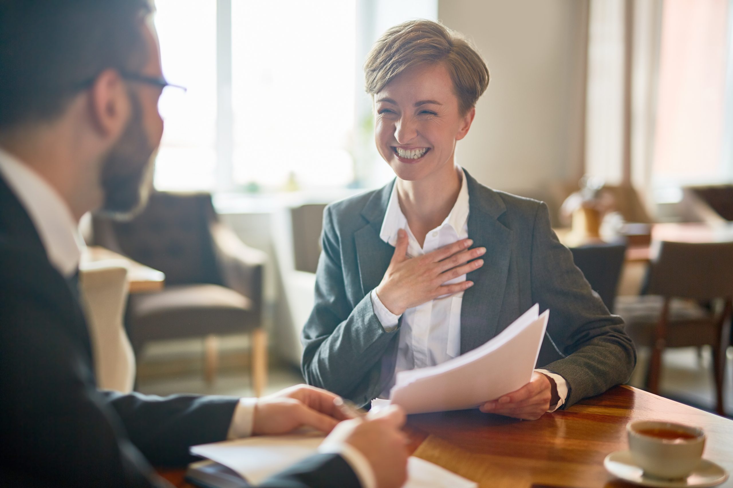 Value-added services concept with excited businesswoman holding papers talking to her advisor at a meeting in cafe.